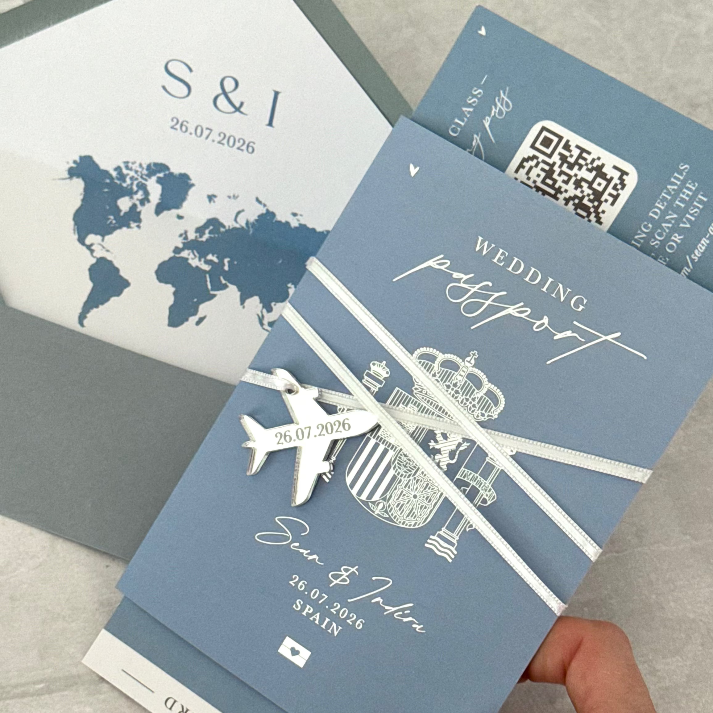 dusty blue and silver passport style wedding invitations for destination wedding with silver metaliic foil and silver acrylic plane charm